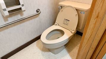 A toilet with a raised seat, a handrail, and a paper towel dispenser.