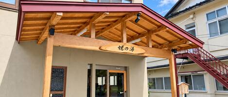 A building with a wooden porch, a sign with Japanese characters, and a staircase leading to the entrance.