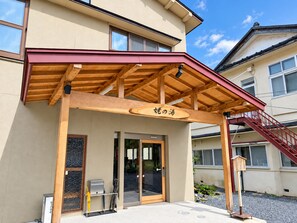 A building with a wooden porch, a sign with Japanese characters, and a staircase leading to the entrance.