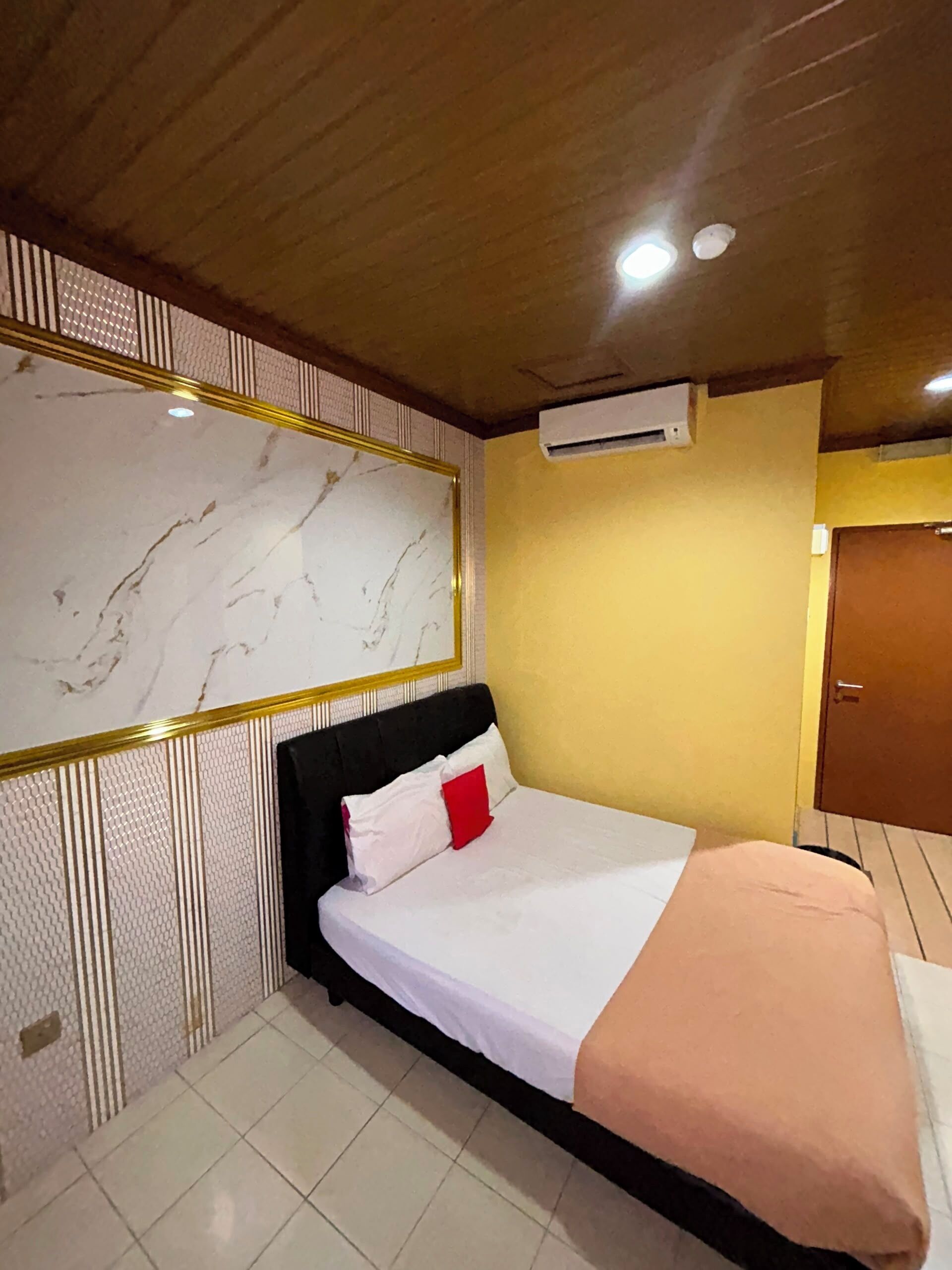 A hotel room with a bed, a wall-mounted air conditioning unit, and a wooden ceiling.