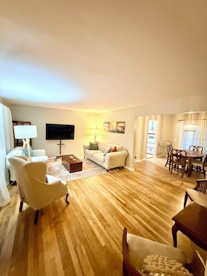 A living room with a sofa, armchairs, a coffee table, a TV, and a dining area with a table and chairs.