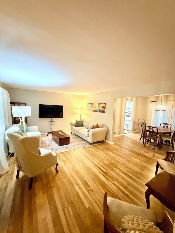 A living room with a sofa, armchairs, a coffee table, a TV, and a dining area with a table and chairs.