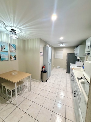 A kitchen with a dining table, cabinets, a refrigerator, and a trash can.