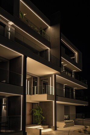 Um edifício com várias andares, varandas, janelas grandes e fachada bem iluminada.