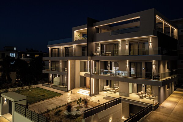 Un edificio moderno de varios pisos con balcones, amplios ventanales y un espacio exterior bien iluminado.