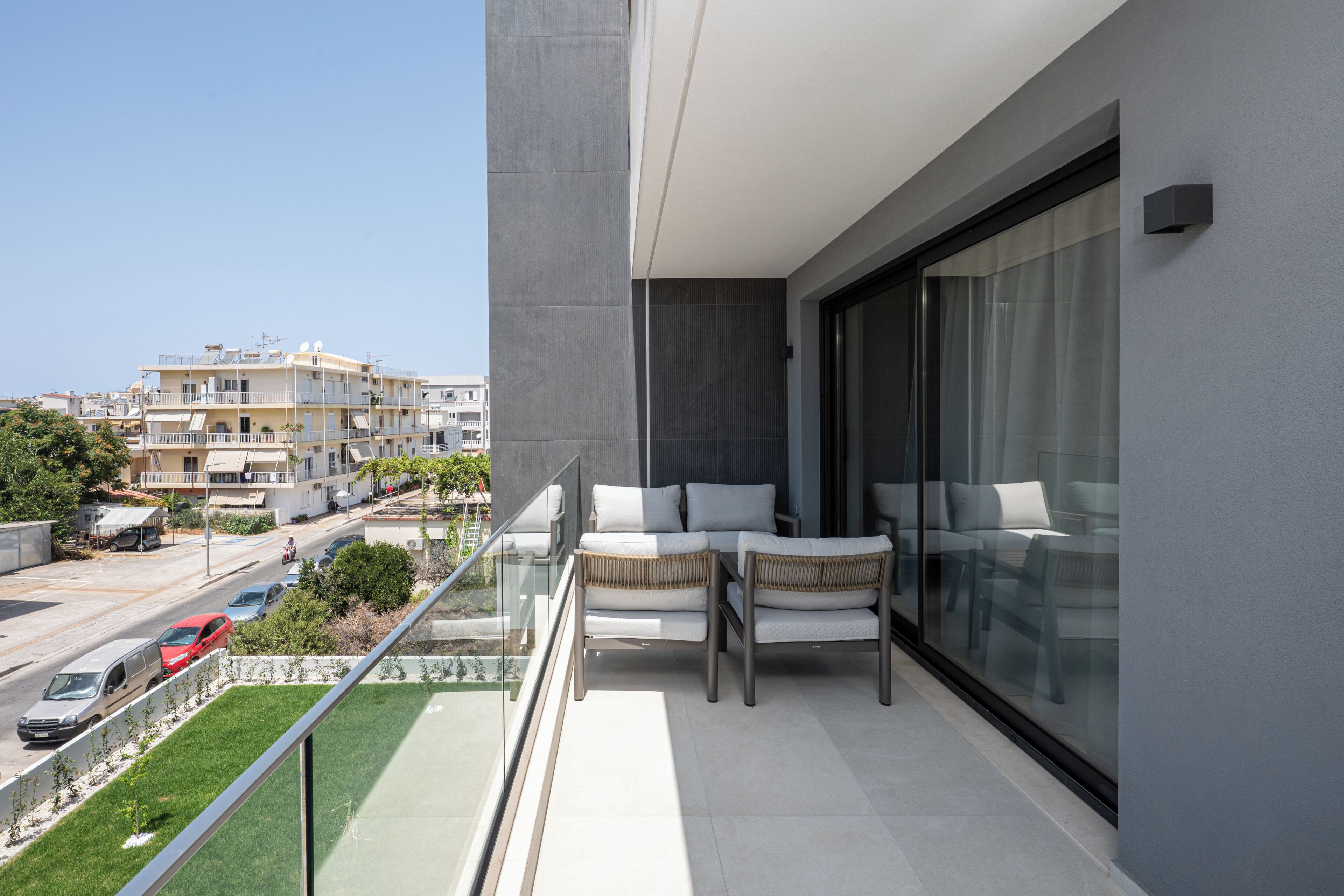 A balcony with a seating area, a view of the street, and a building in the background.