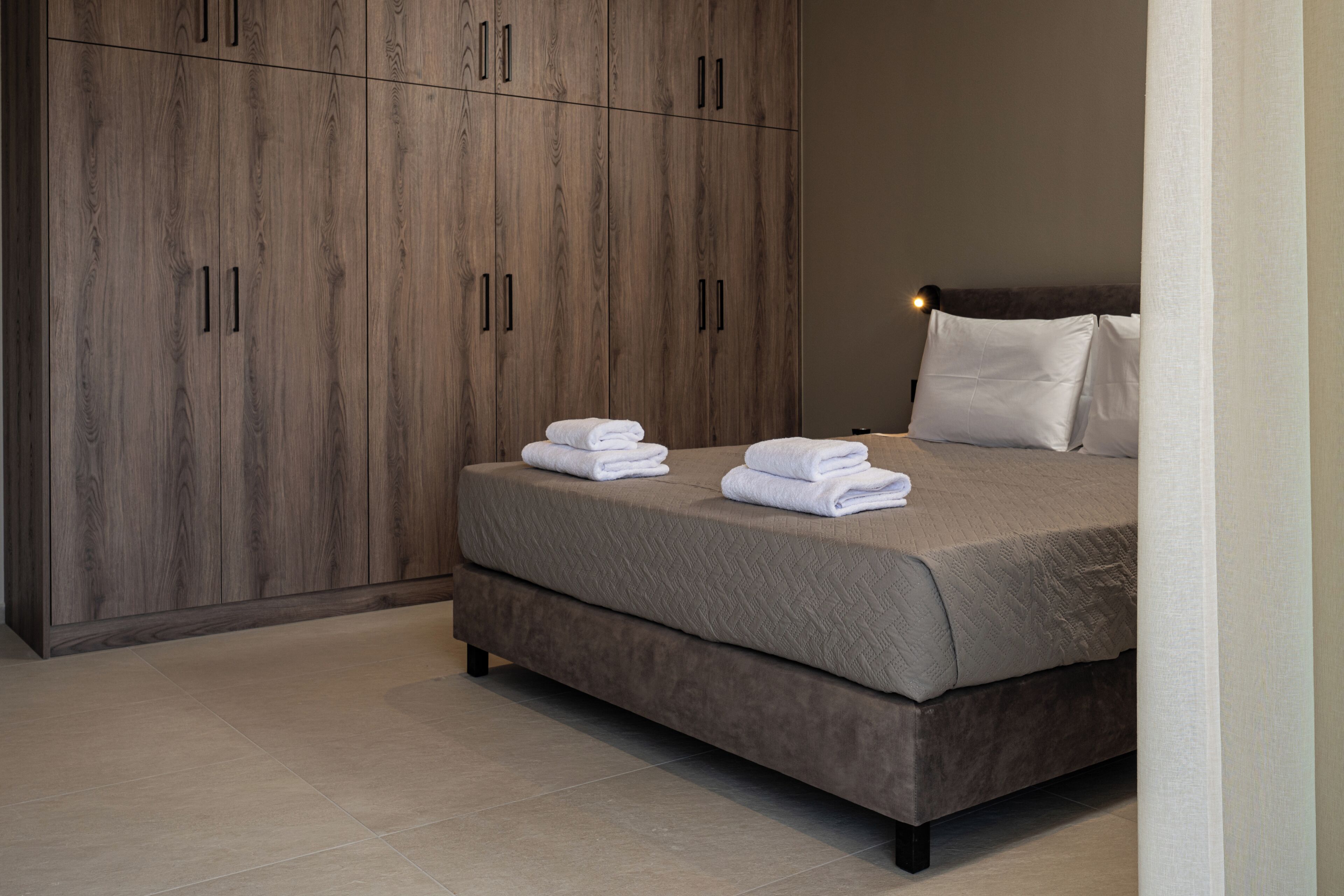 A bedroom with a large wardrobe, a bed with a quilted cover, and neatly folded towels.