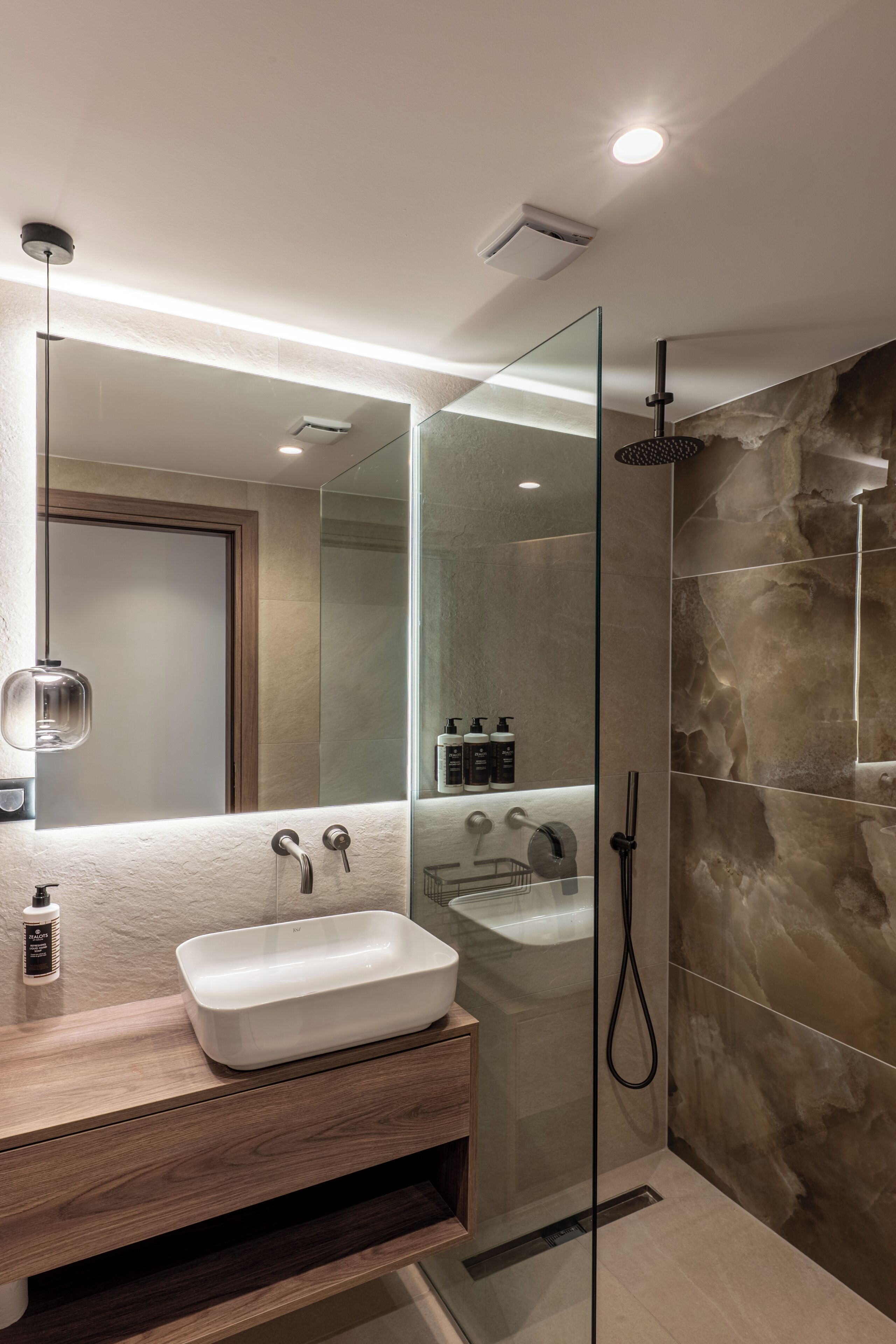 A modern bathroom with a glass-enclosed shower, a white sink, and a large mirror.