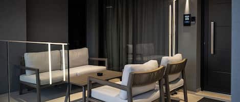 Una sala de estar moderna con un sofá, sillas y una mesa de centro. Hay una partición de vidrio y una puerta con un letrero que indica el número de habitación 103.