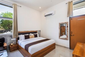 Ein Hotelzimmer mit Bett, Nachttisch, Lampe, Klimaanlage und Spiegel an der Wand.