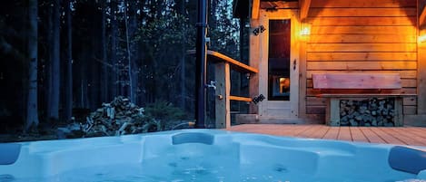 A hot tub with a wooden deck, surrounded by a forest.