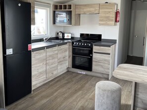 A compact kitchen with a black refrigerator, a microwave, a stove, and wooden cabinets. - Haven Seashore, Ellerton Willerby Xtra (Great Yarmouth)