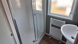 Ein Badezimmer mit Duschkabine aus Glas, einem weißen Waschbecken und einem Heizkörper.