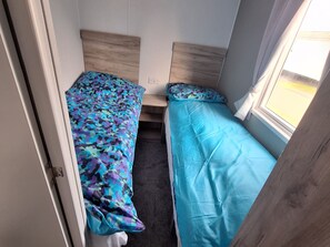 A small room with two beds, a window, and a door. - Haven Seashore, Ellerton Willerby Xtra (Great Yarmouth)