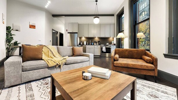 A modern living room with a grey sofa, a brown armchair, and a wooden coffee table. - Comfortable 2BR — Conveni (Pittsburgh)