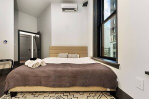 Une chambre d’hôtel avec un lit, une fenêtre, un appareil de climatisation et une vue sur la ville.