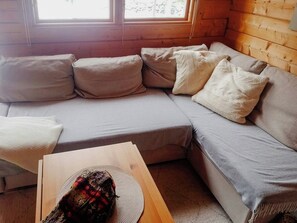 Ein gemütliches Blockhaus-Interieur mit einer Eckcouch, einem Holztisch und einem Fenster mit Jalousien.