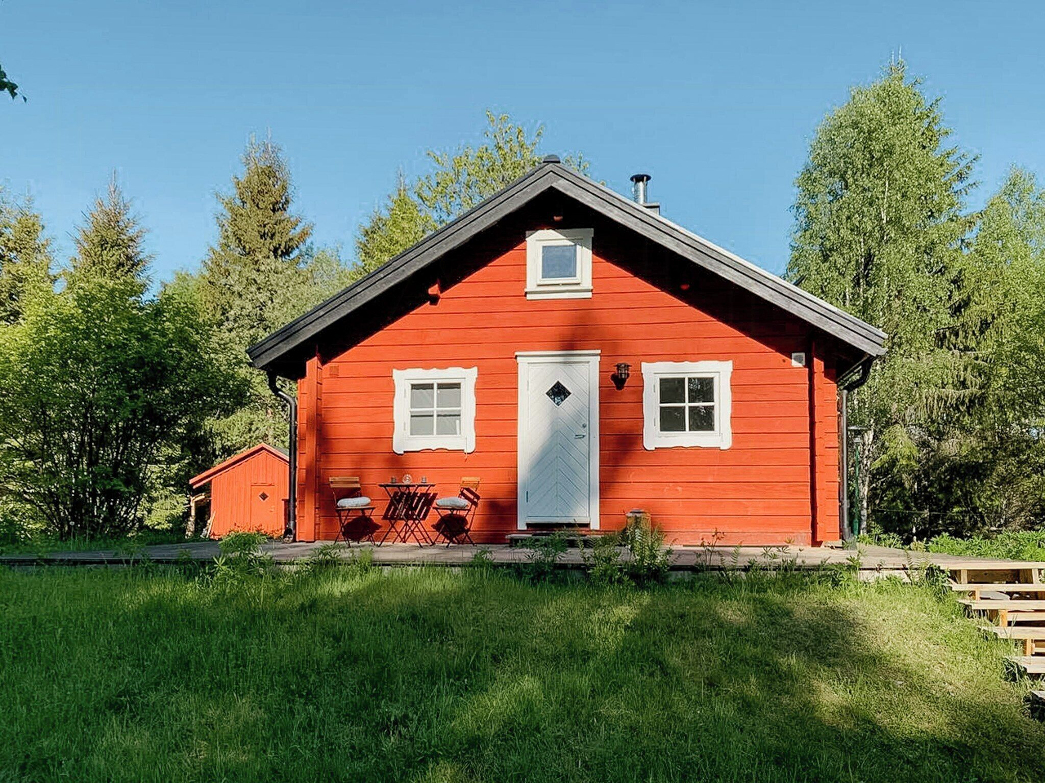 Ein rotes Holzhaus mit Satteldach, einer Haustür und zwei Fenstern.