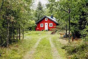Ett rött hus med en vit dörr och vita fönster, omgivet av träd och en gräsbevuxen stig som leder fram till det.