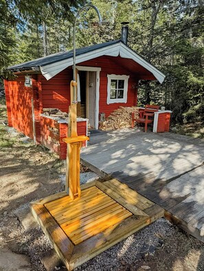 A red cabin with a chimney, a wooden bench, and a fire pit area. - Log cabin with hot tub and nature right outside (Ryd)