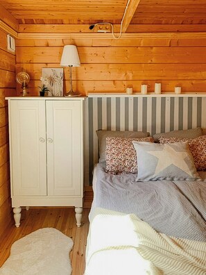 A wooden cabin interior with a bed, a white cabinet, and a radiator. - Log cabin with hot tub and nature right outside (Ryd)