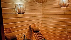 Ein Saunaraum mit Holzwänden und -bänken, einem kleinen Tisch und zwei Wandleuchten.