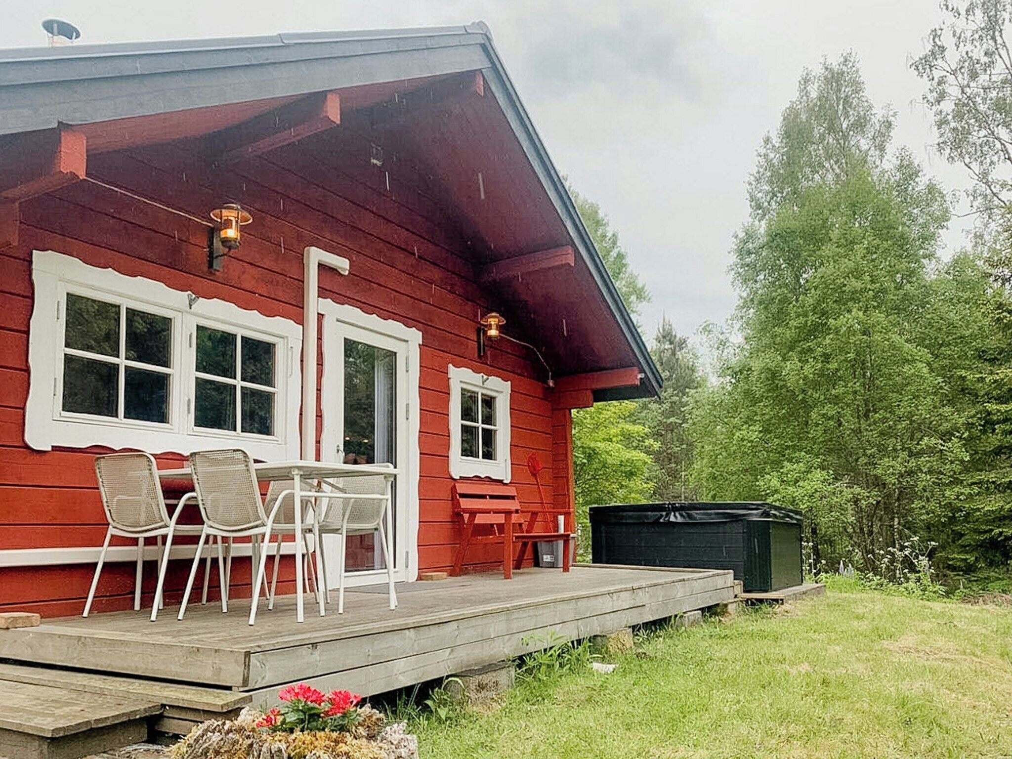A red wooden house with a porch, two white-framed windows, and a small table with chairs.