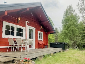 Ein rotes Holzhaus mit Veranda, zwei Fenstern mit weißen Rahmen und einem kleinen Tisch mit Stühlen.