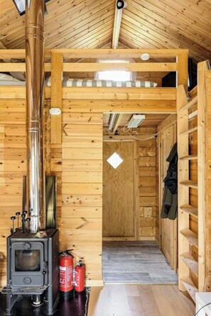 Ein Holzhütten-Interieur mit Kaminofen, Schornstein und einer Tür zu einem anderen Raum.