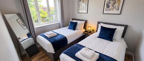 A hotel room with two beds, a window with curtains, a mirror, and framed artwork on the wall.