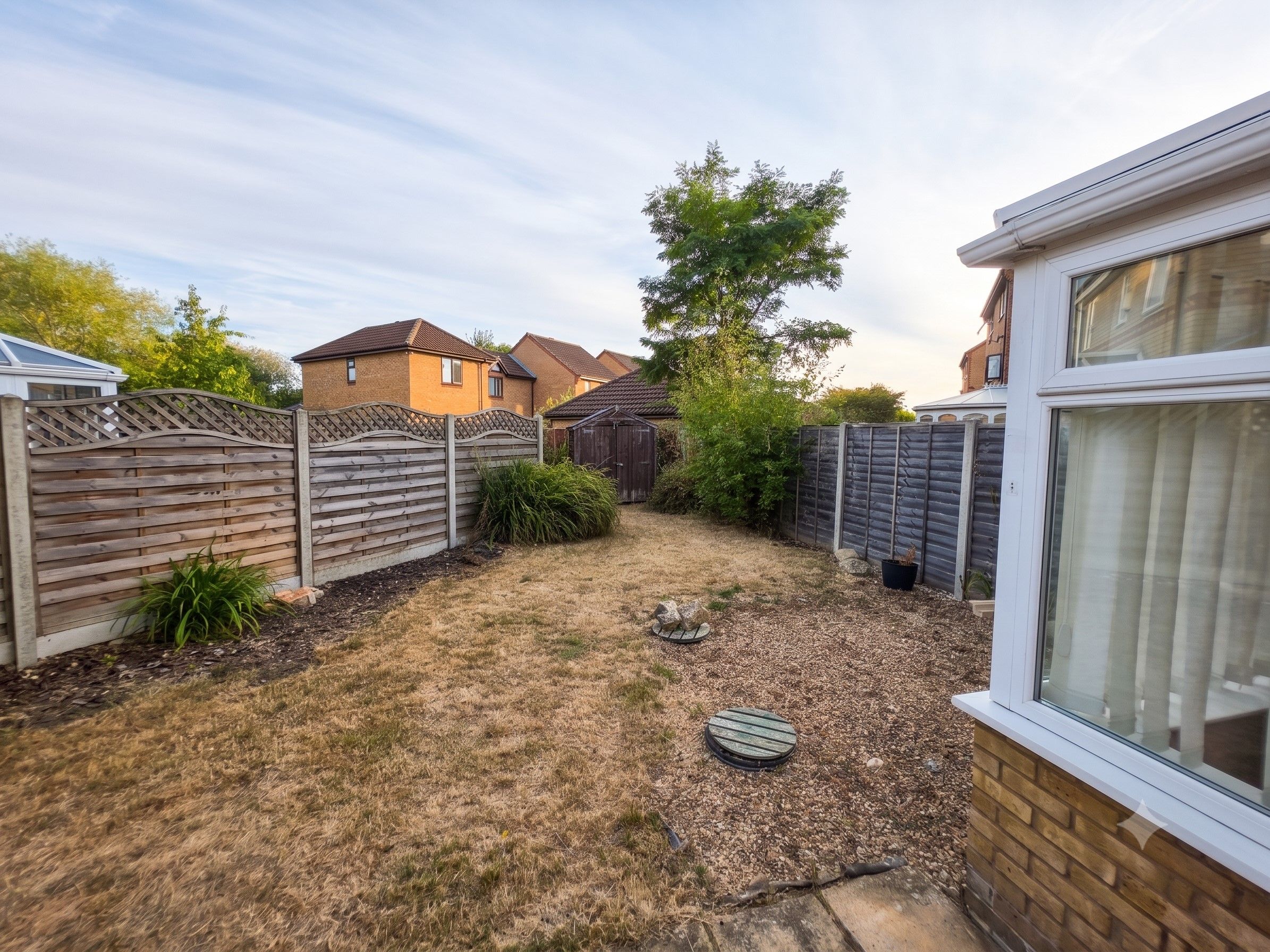 A residential backyard with a wooden fence, a small shed, and a grassy area with mulch.