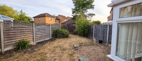 A residential backyard with a wooden fence, a small shed, and a grassy area with mulch.