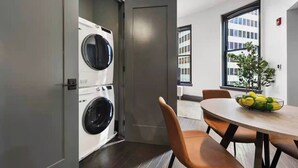 A modern apartment with a laundry area, a dining table with chairs, and a view of a building through a window. - Cozy 1BR Downtown Pittsbu (Pittsburgh)