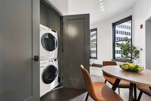 A modern apartment with a laundry area, a dining table with chairs, and a view of a building through a window. - Cozy 1BR Downtown Pittsbu (Pittsburgh)