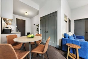 Una sala de estar moderna con una mesa redonda, sillas color naranja, un sofá azul y un taburete de madera.