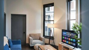 A modern living room with a sofa, armchair, coffee table, lamp, TV, and a view of the outside. - Cozy 1BR Downtown Pittsbu (Pittsburgh)