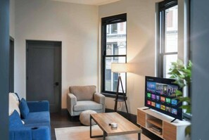 A modern living room with a sofa, armchair, coffee table, lamp, TV, and a view of the outside. - Cozy 1BR Downtown Pittsbu (Pittsburgh)
