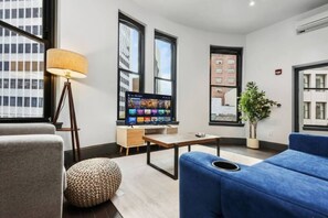 A modern living room with a flat-screen TV, a lamp, a sofa, and a potted plant. - Cozy 1BR Downtown Pittsbu (Pittsburgh)