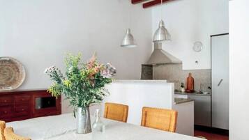 Un comedor con una mesa, sillas, un jarrón con flores y una cocina al fondo.