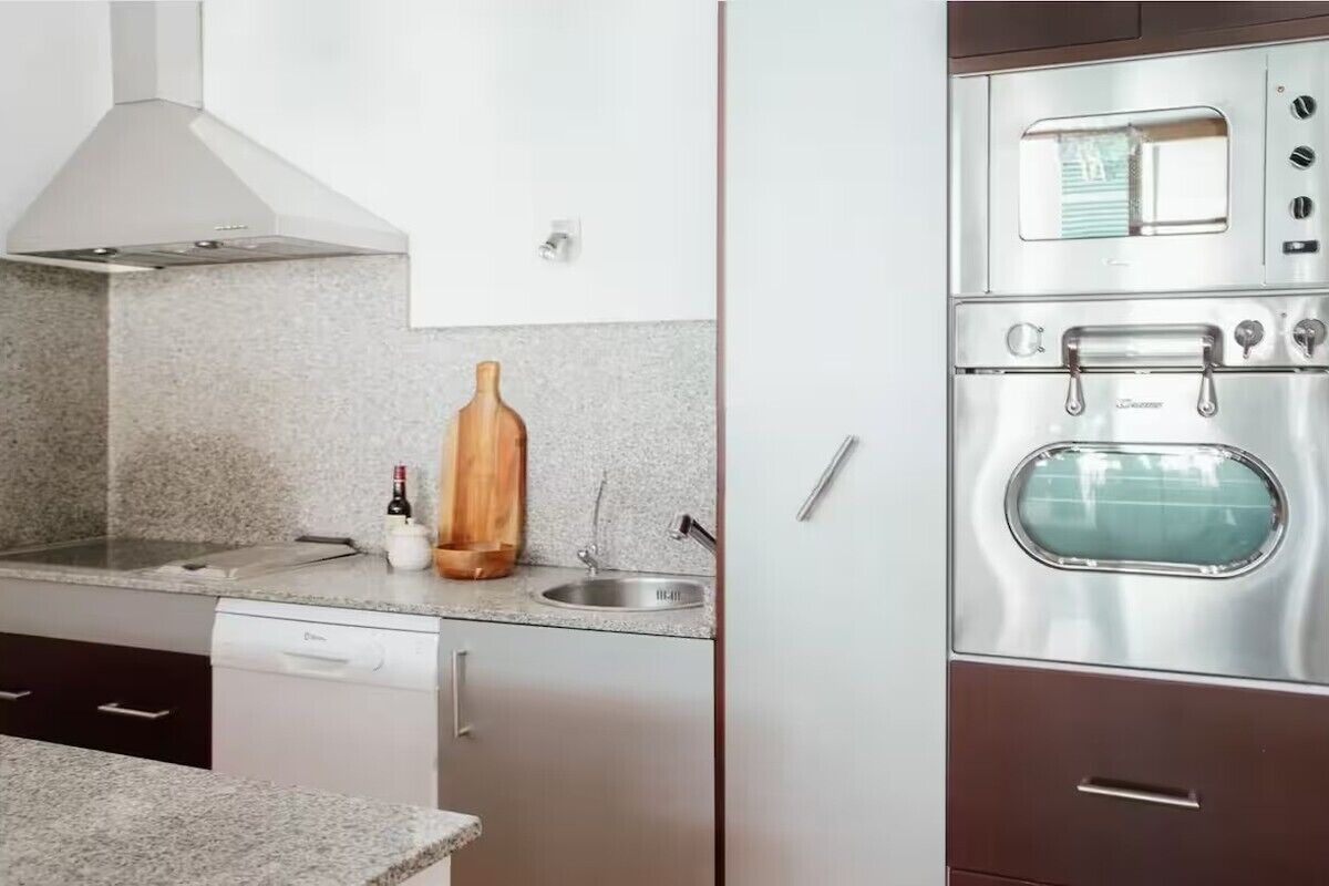 Een keuken met een inbouwoven, een roestvrijstalen afzuigkap en een granieten aanrecht.