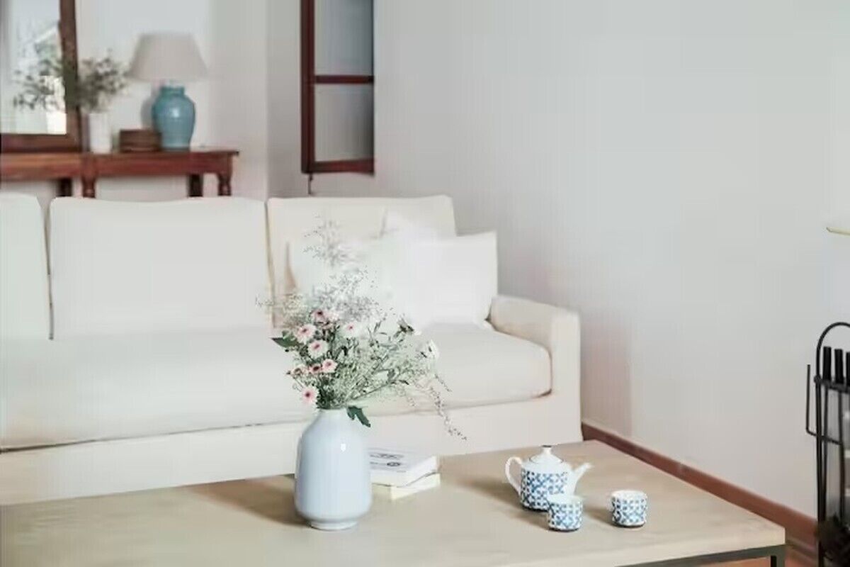 Een woonkamer met een witte bank, een salontafel met een bloevas en een boekenkast.