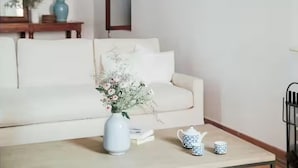 A living room with a white sofa, a coffee table with a vase of flowers, and a bookshelf.