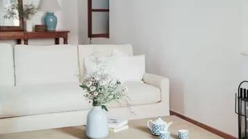 Een woonkamer met een witte bank, een salontafel met een bloevas en een boekenkast.