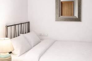 A neatly made bed with white bedding, a black metal headboard, a bedside lamp, and a wall-mounted mirror with a decorative frame.
