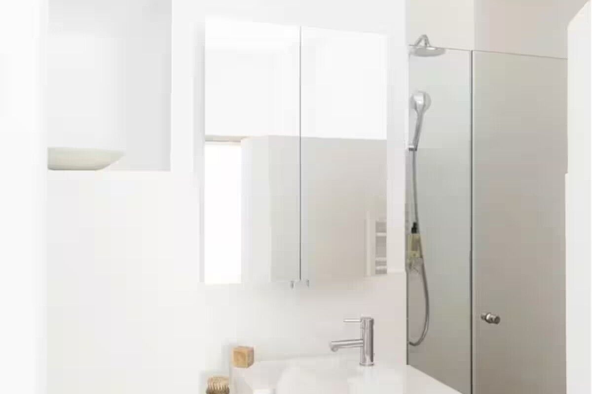Ein modernes Badezimmer mit einem weißen Waschtisch, einer Duschkabine und einem Spiegel.