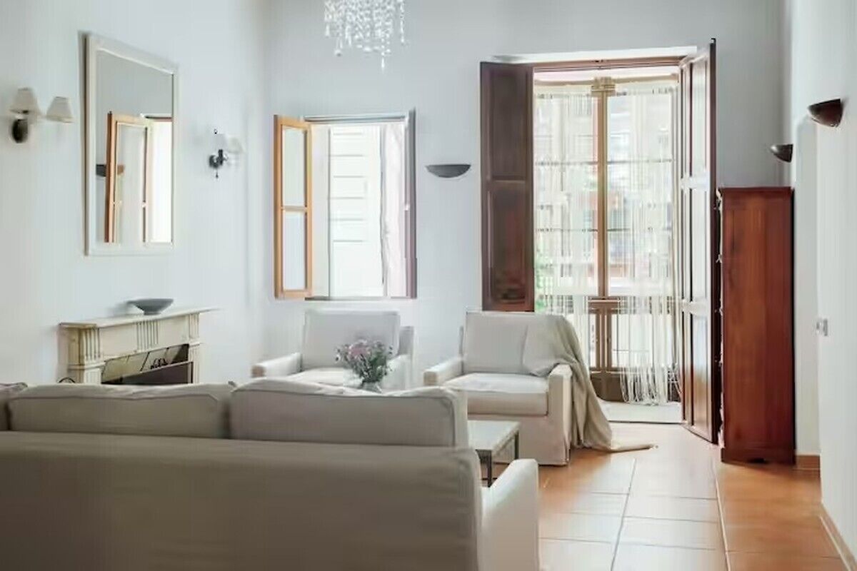 Ein Wohnzimmer mit einer Couch, Sesseln, einem Kamin und einem großen Fenster mit Vorhängen.
