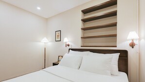 Una cama bien tendida con sábanas blancas, un cabecero de madera y dos lámparas de noche.