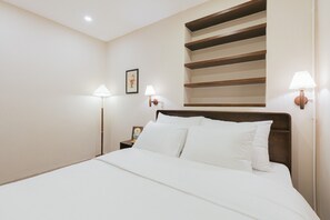 A neatly made bed with white linens, a wooden headboard, and two bedside lamps. - Lily Hidden Homestay Spacious 150m² 2BR near Hoan Kiem Lake (Hanoi, Vietnam)