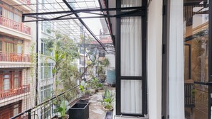 Un balcón estrecho con plantas en macetas, baranda de metal y vistas a edificios vecinos.