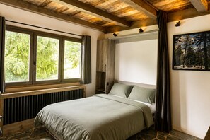 Ein Schlafzimmer mit Bett, Fenster, Heizkörper, einem Gemälde und einer Holzzieldecke.